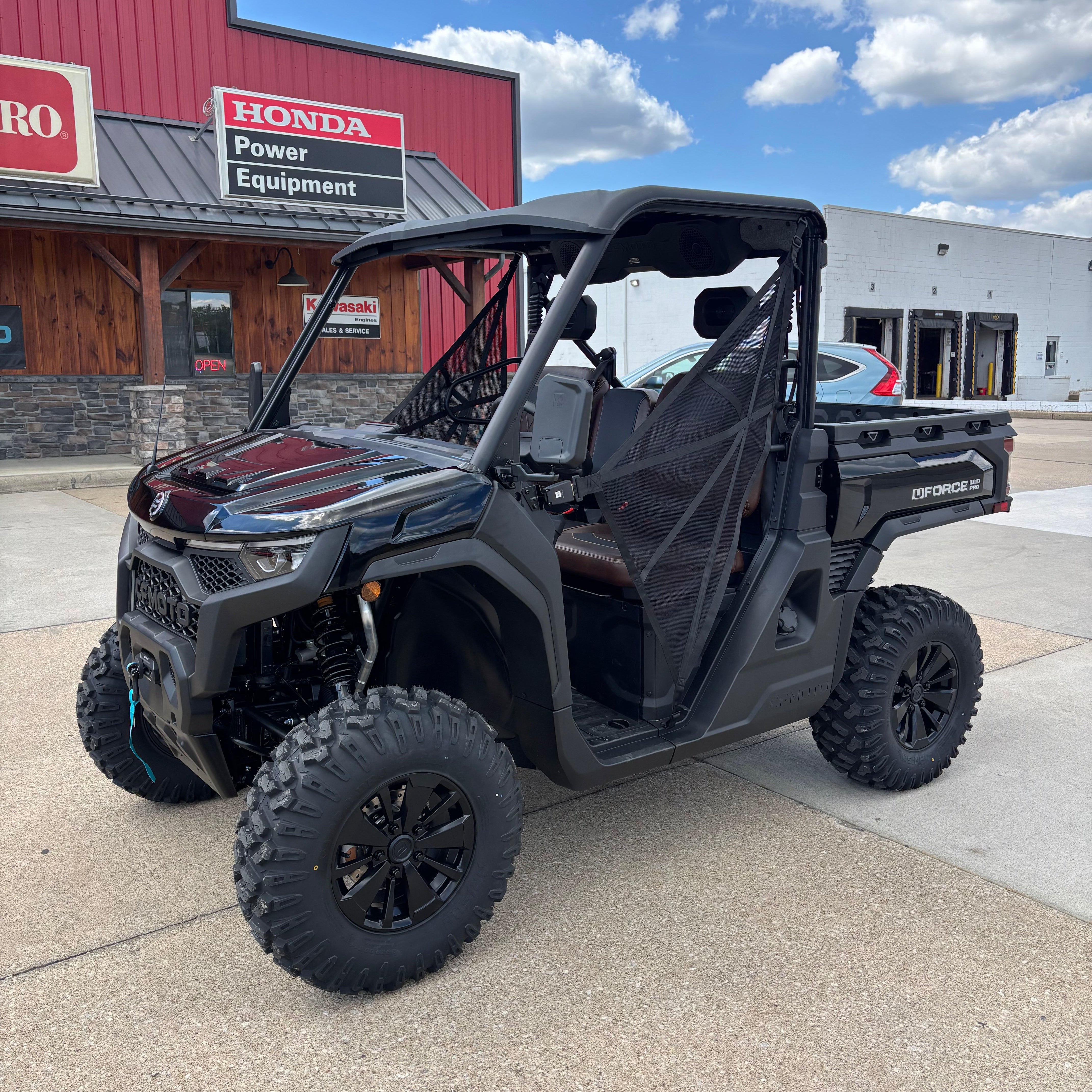 Black off-road vehicle parked on a concrete surface with a building and blue sky in the background.